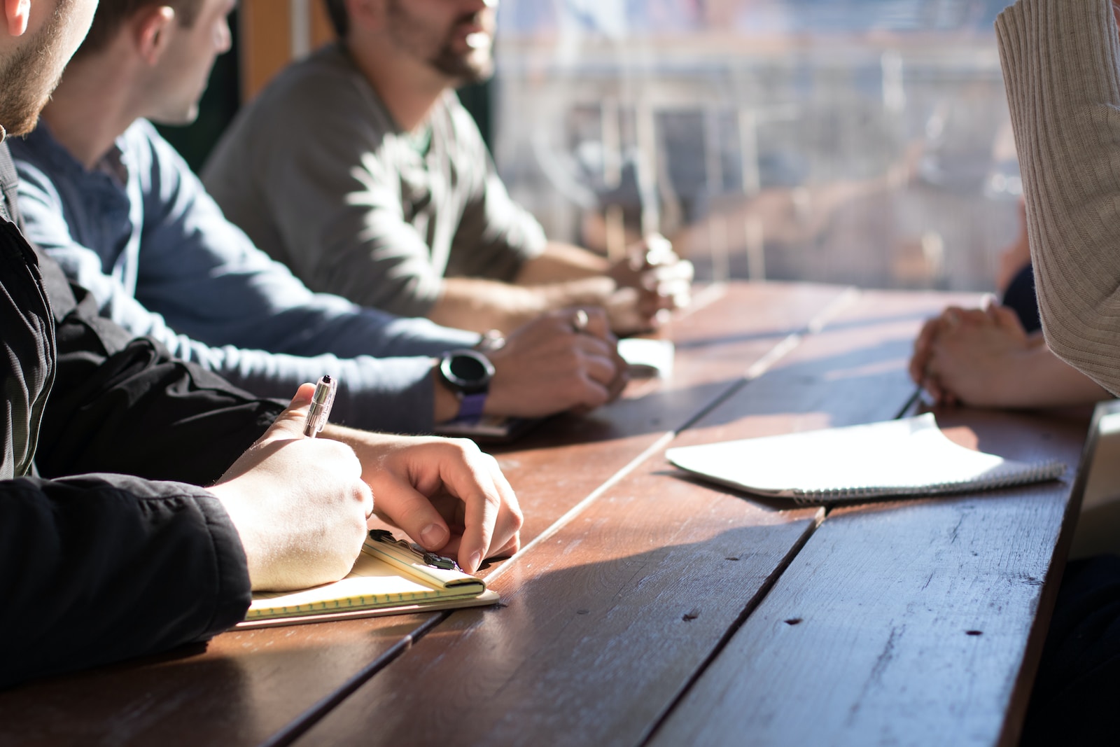 people sitting on chair in front of table while holding pens during daytime in business meeting